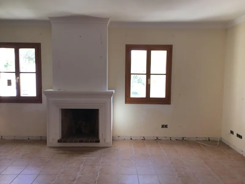 Antes: salón con chimenea blanca, suelo de terracota y ventanas de madera