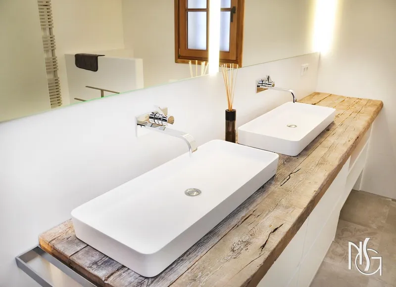 Baño con dos lavabos blancos sobre encimera de madera recuperada