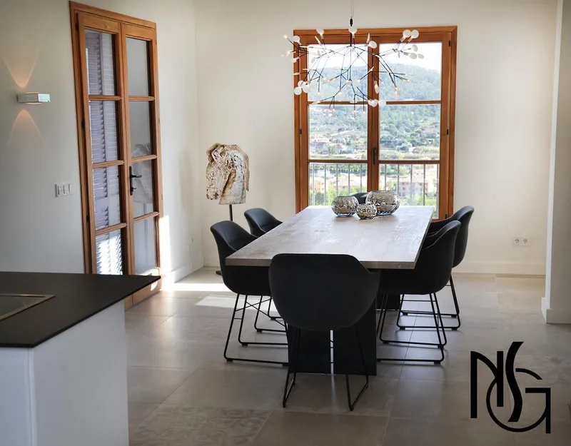 Comedor con mesa de madera, sillas negras y ventanales de madera con vistas