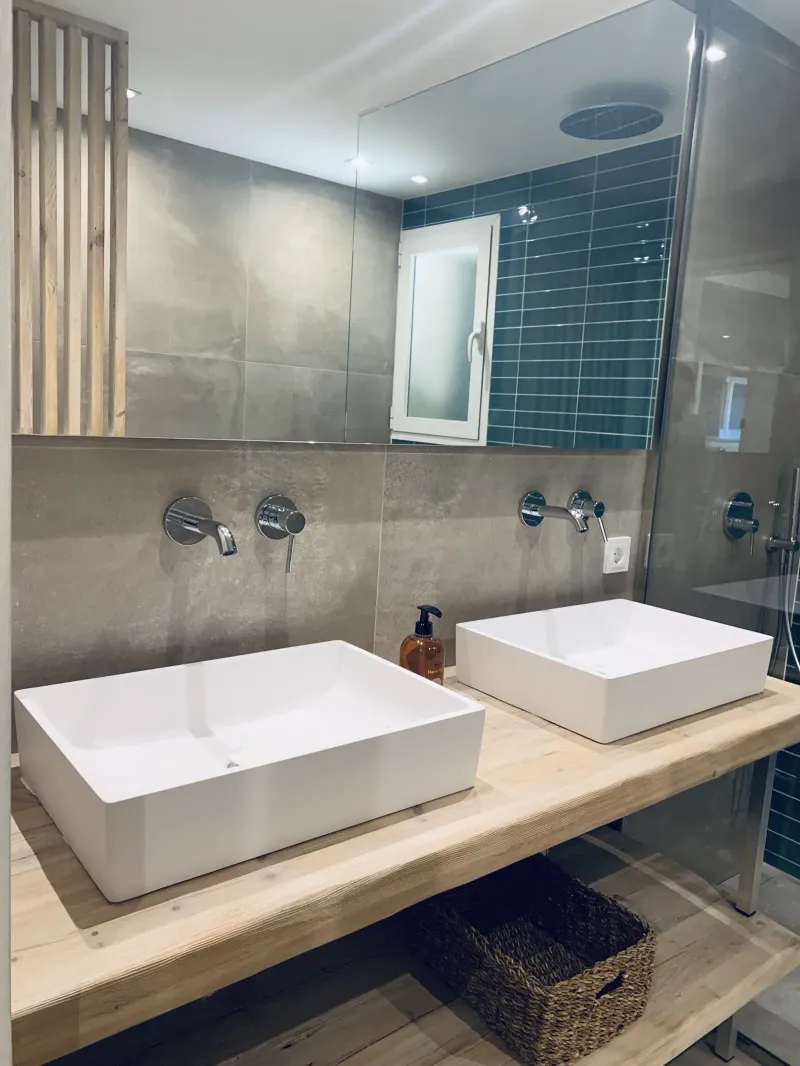 Baño con dos lavabos sobre madera natural y ducha de azulejo azul
