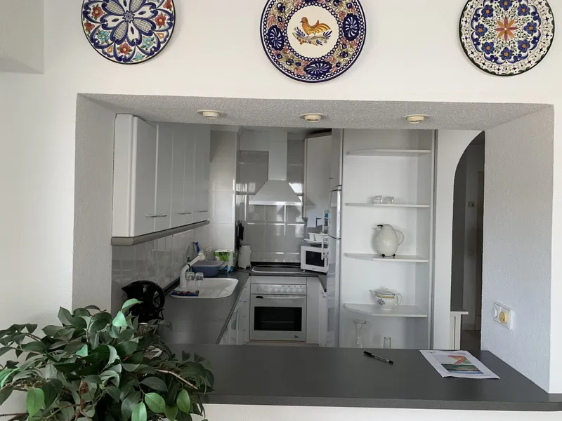 Antes: cocina con muebles blancos, platos decorativos en la pared y barra