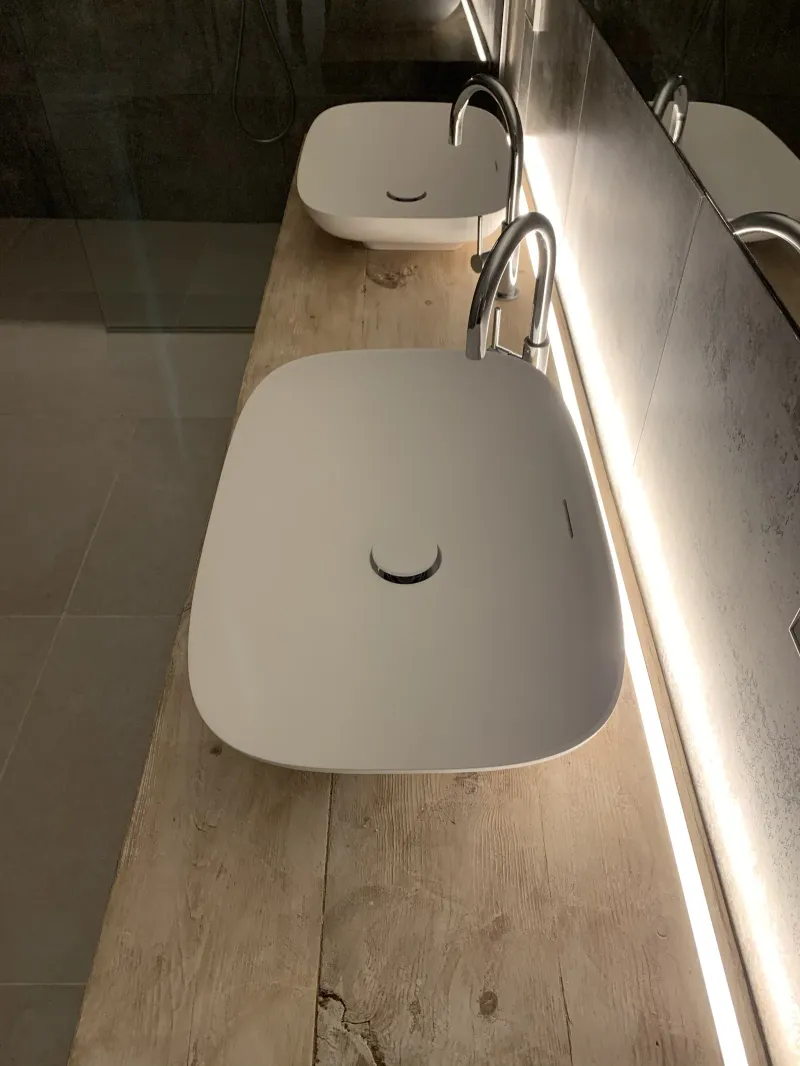 Lavabo ovalado sobre madera junto a una línea de luz