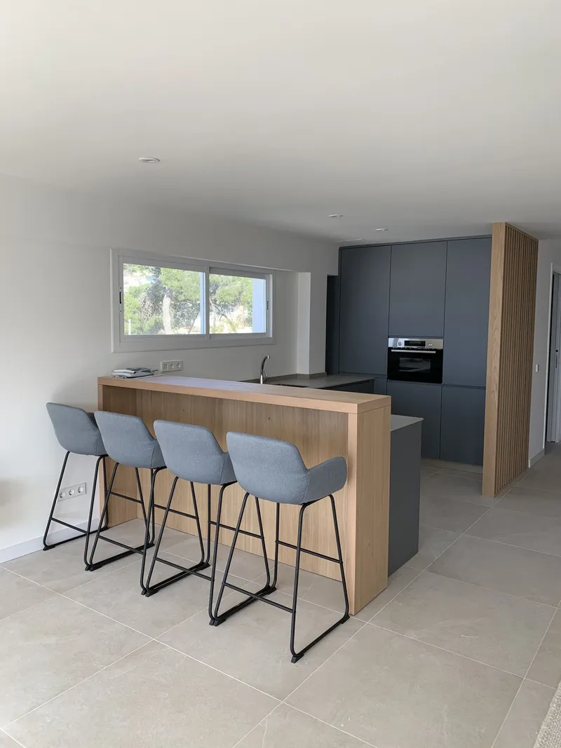 Cocina gris con barra de madera, taburetes azul claro y ventana