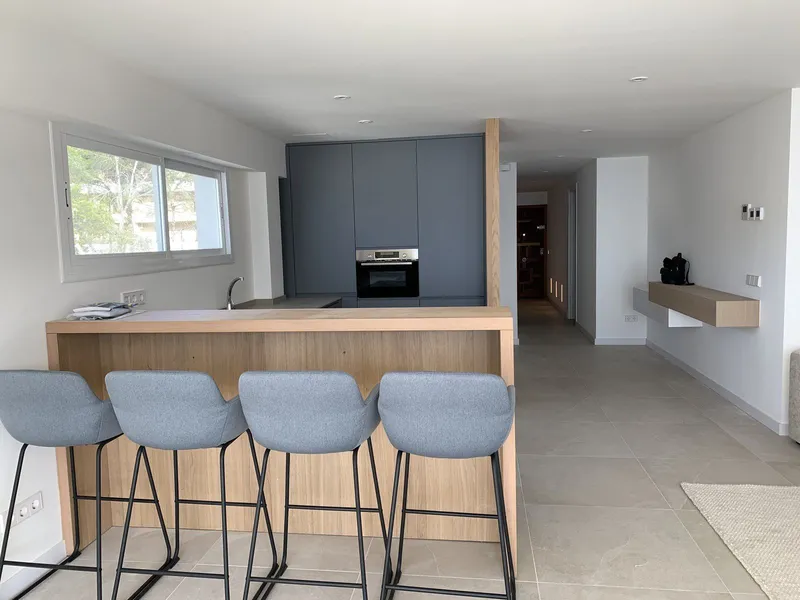Después: cocina gris con barra de madera, taburetes y pasillo al fondo