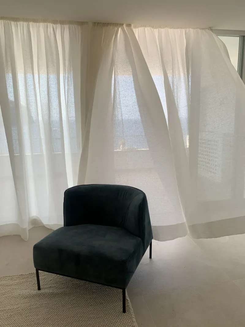 Butaca azul petróleo junto a cortinas de lino