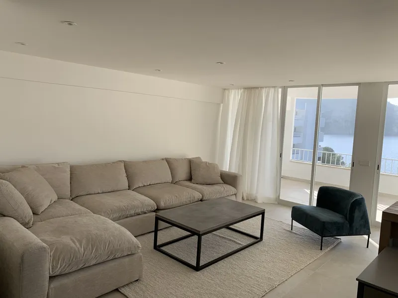 Salón con sofá claro, mesa de centro de hierro y ventanales al mar