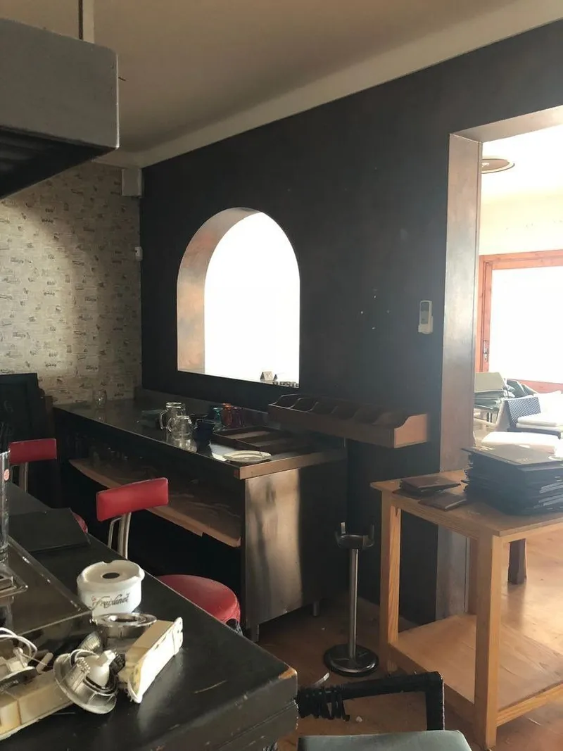 Antes: sala con pared oscura, ventana en arco y taburetes rojos