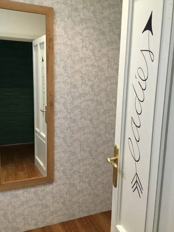 Puerta del baño de señoras con espejo y papel pintado