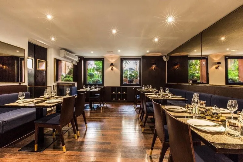 Comedor con bancos azul oscuro, sillas de madera, espejos y apliques cálidos
