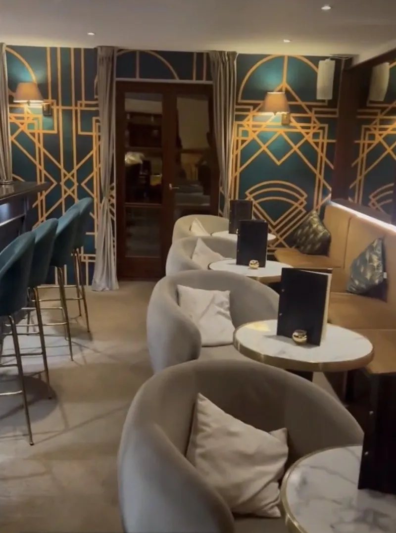 Butacas de terciopelo gris y pared art déco en verde y oro junto a la barra