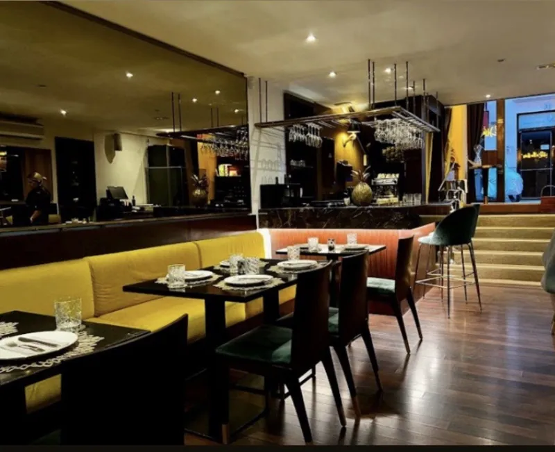 Sala con banco amarillo mostaza, sillas verdes y barra al fondo