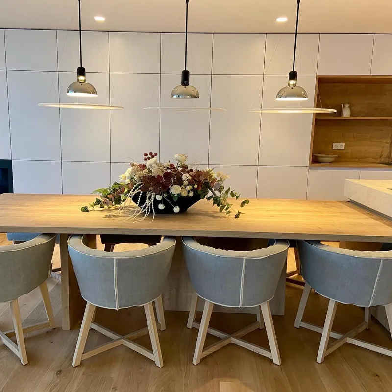 Mesa de comedor de madera con centro floral, lámparas colgantes y cocina blanca