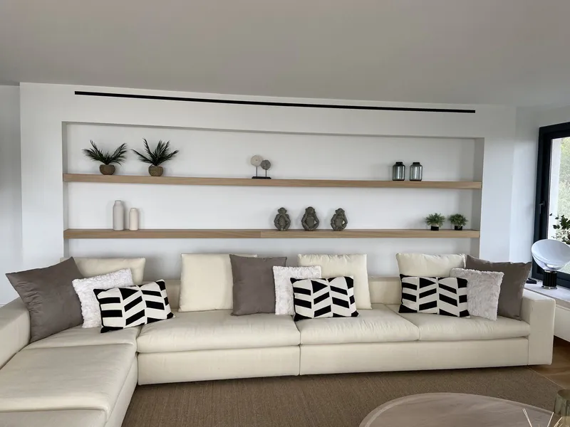 Sofá con cojines en blanco y negro bajo estantes iluminados con jarrones