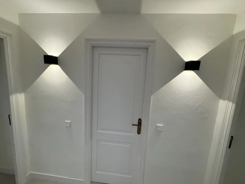 Puerta blanca entre dos apliques que proyectan luz en la pared