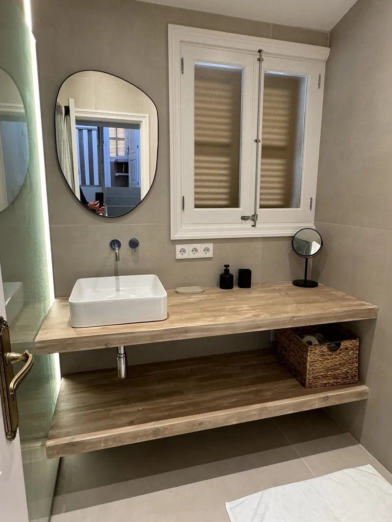 Baño con espejo orgánico, encimera de madera flotante y luz verde indirecta
