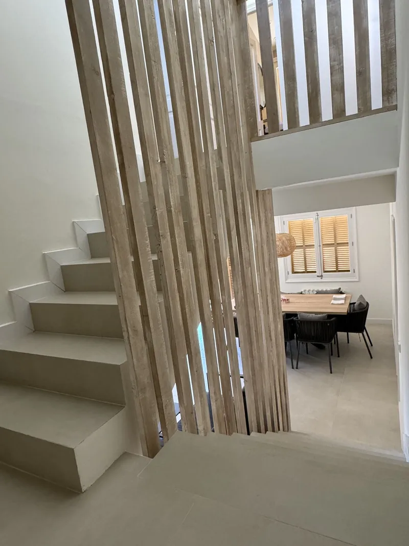 Escalera blanca con celosía de lamas de madera y comedor al fondo