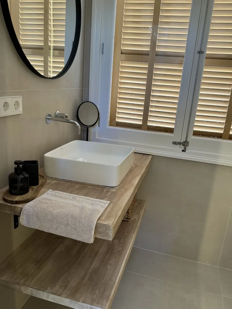 Lavabo sobre encimera de madera con espejo redondo y contraventanas de madera