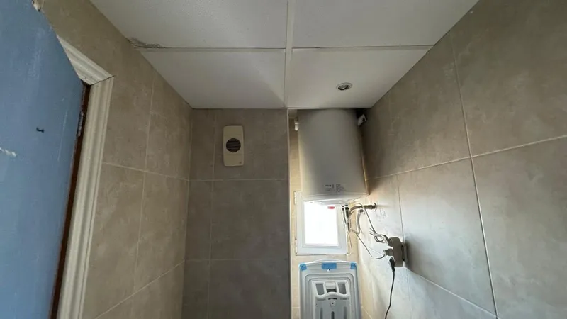 Antes: baño con revestimiento gris y termo a la vista