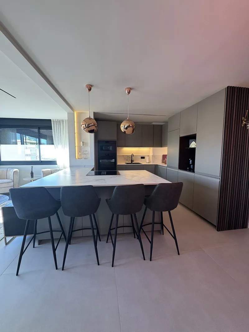Cocina abierta con isla, sillas grises, lámparas de cobre y panel de madera acanalada