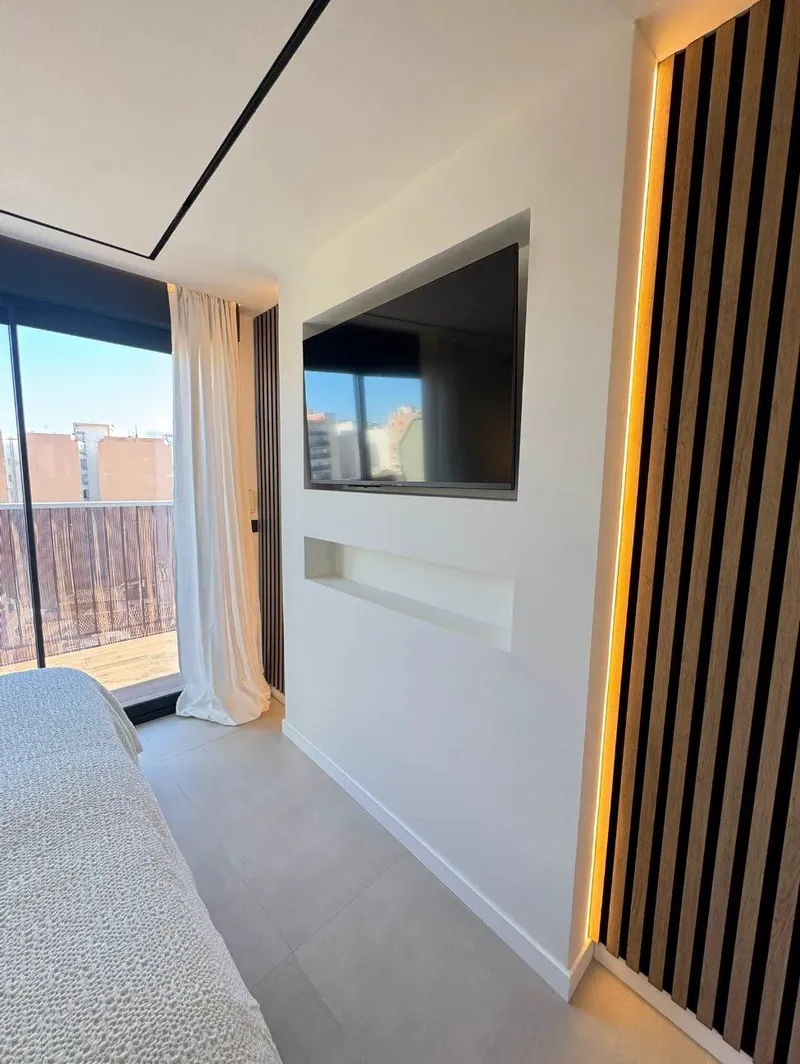 Después: dormitorio con pared de listones de madera iluminada y nicho para televisión