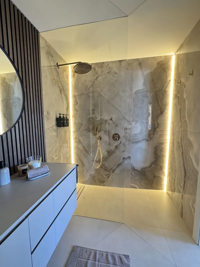 Después: ducha de obra con perfiles de luz cálida y revestimiento veteado