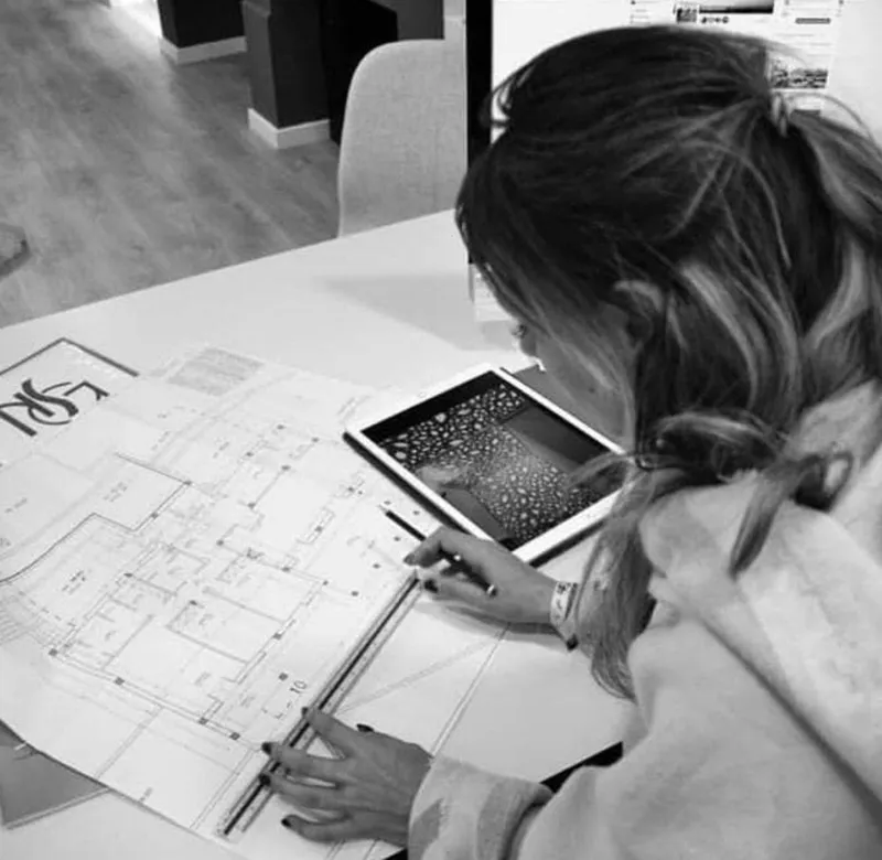 Nathalie dibujando sobre un plano con una tableta al lado, en blanco y negro