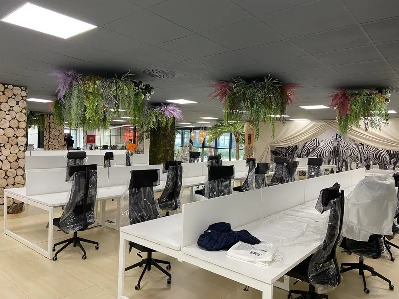 Mesas operativas blancas con columnas de troncos y vegetación en el techo