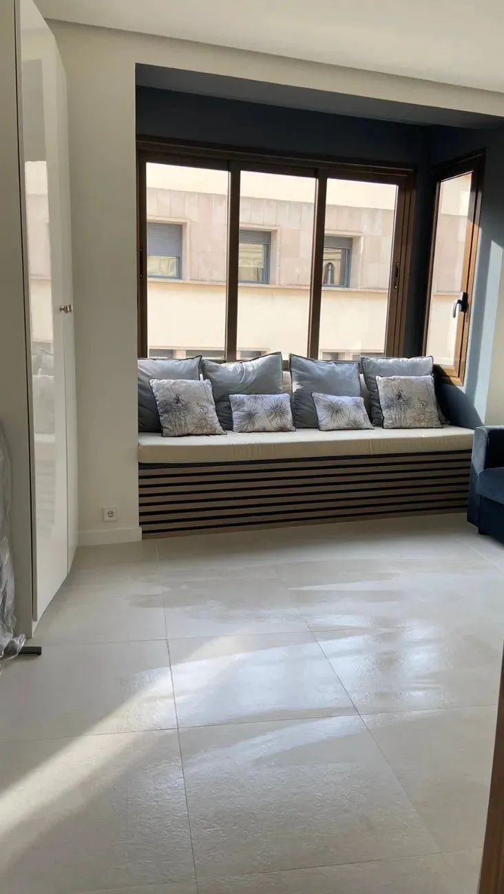 Banco bajo la ventana con cojines estampados y suelo claro de gran formato