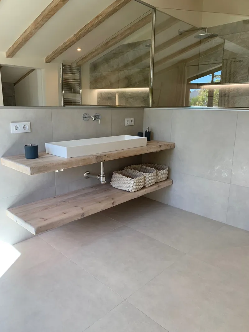 Baño con lavabo doble sobre encimera de madera, espejo amplio y luz indirecta