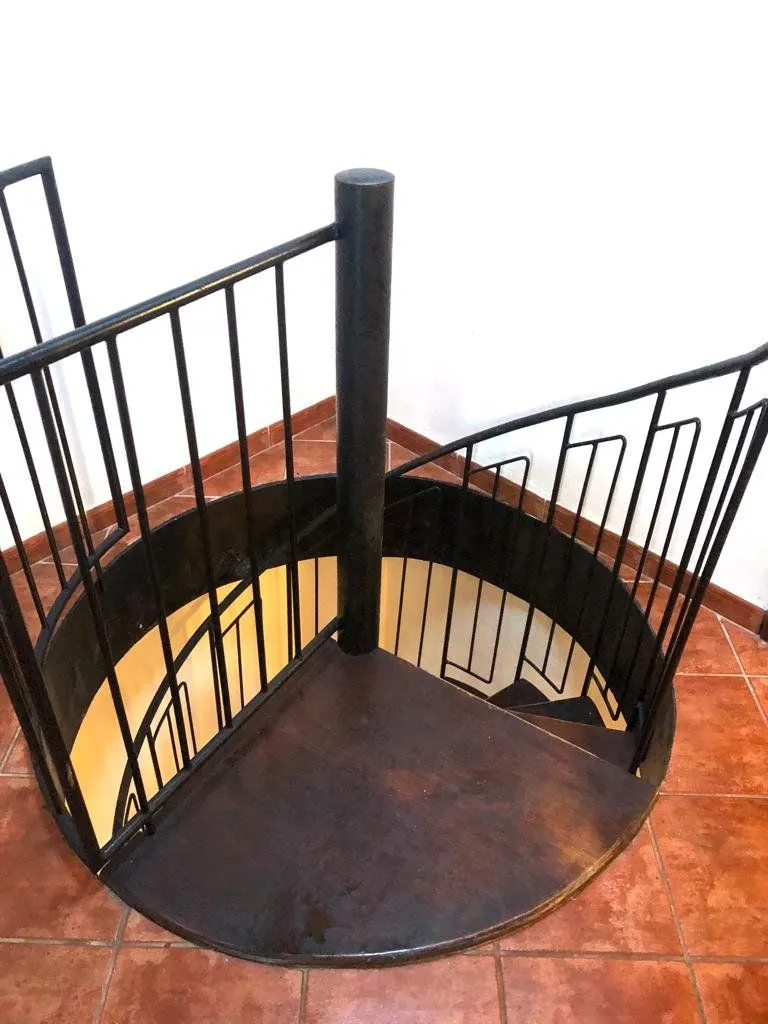 Antes: escalera de caracol de hierro oscuro sobre suelo de terracota
