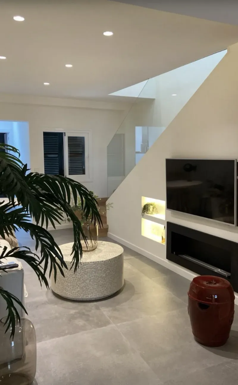 Salón con televisor y nichos iluminados bajo la escalera y cerámica en rojo oscuro