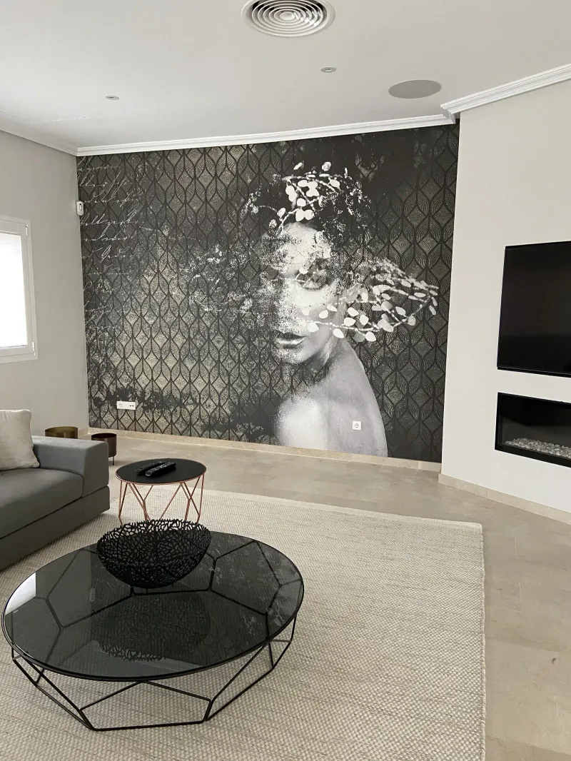 Mural en blanco y negro de un rostro de mujer sobre fondo geométrico, con mesa de centro de cristal