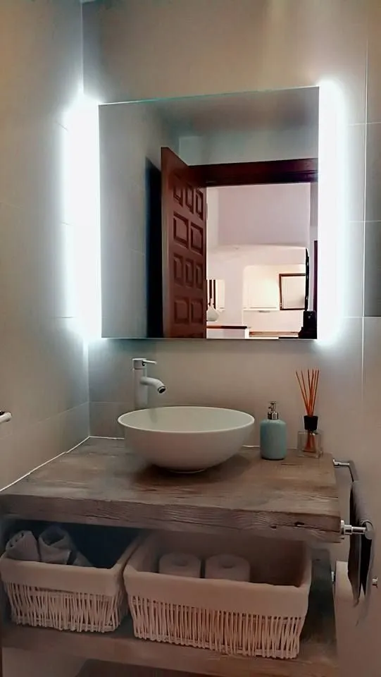 Aseo de invitados reformado con baldas de madera y espejo iluminado
