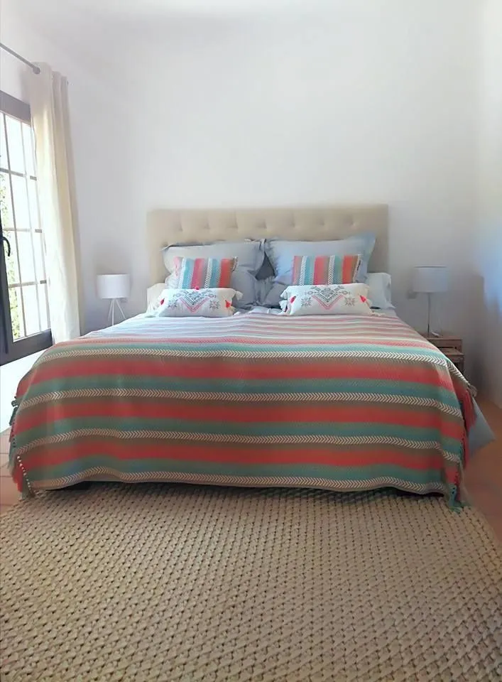 Habitación de invitados con cama crema y textiles de colores vivos